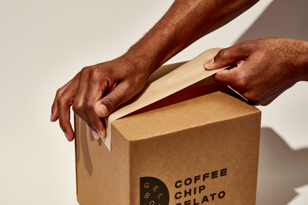 Hands using water activated gummed paper tape to seal a shipping box.
