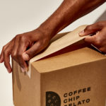 Hands using water activated gummed paper tape to seal a shipping box.
